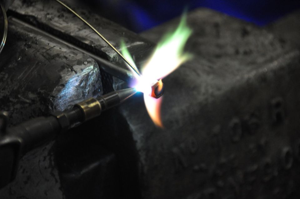 Close-up of a torch flame heating a small metal piece held in a vise