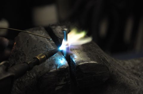 1996 Ford Bronco - A torch is used to heat a screw held in a vise.