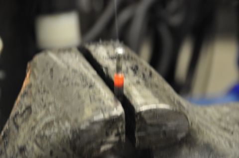 1996 Ford Bronco - A close-up view shows a metal vise holding a heated rod, with indistinct objects in the background.