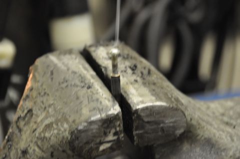 1996 Ford Bronco - A small metal component is secured in a vise for work, with a wire attached.
