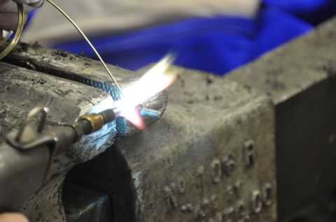 1996 Ford Bronco - A torch heats a metal part secured in a vise, with a blue cloth in the background.