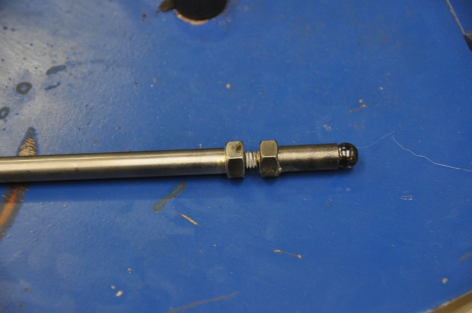 Metal rod with two nuts and a rounded end, resting on a blue surface
