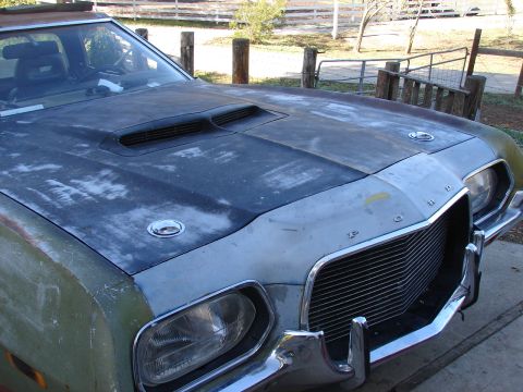 1973 Ford Ranchero - The front of a 1973 Ford Ranchero shows a prominent hood scoop and a distinctive chrome grille, with weathered paint.