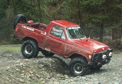 1982 Ford Bronco - Red Ford Bronco with off-road modifications navigates a rocky incline.
