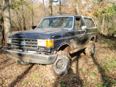 1990 Ford Bronco - This Ford Bronco is deep in the mud, surrounded by trees and fallen leaves.