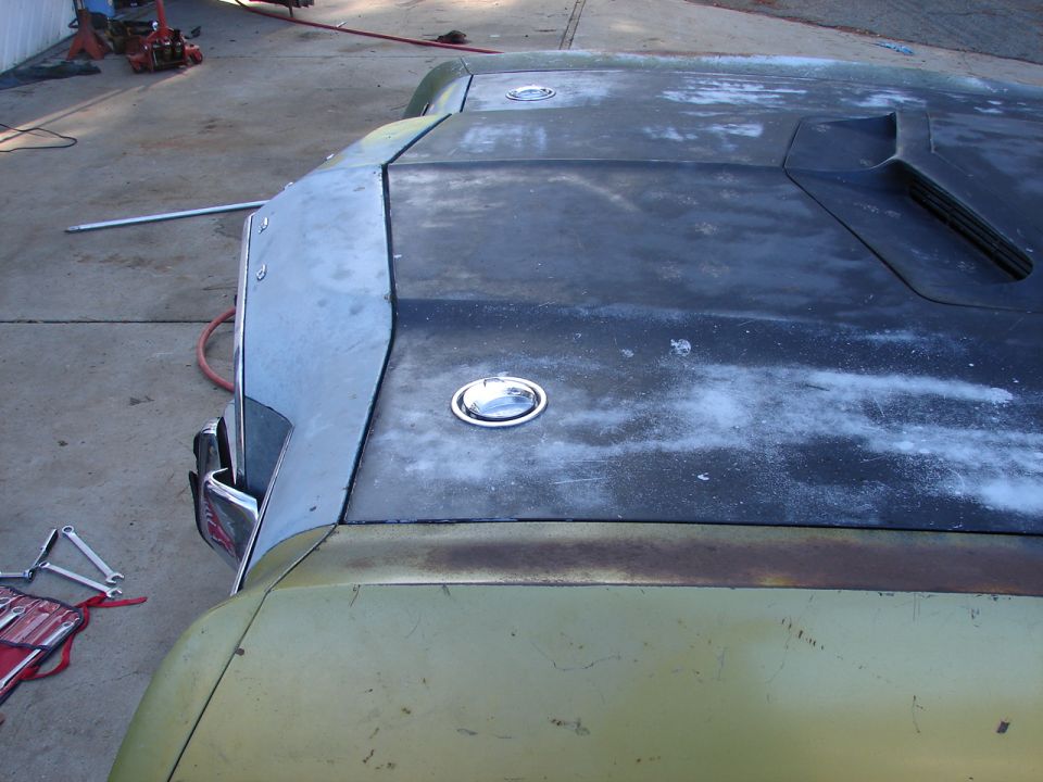 Car hood with two flush-mount gas caps and a hood scoop, showing primer and rust damage