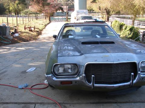 1973 Ford Ranchero - A weathered 1972 Ford Ranchero sits on a concrete driveway, its hood showing primer gray and its fenders a faded green.