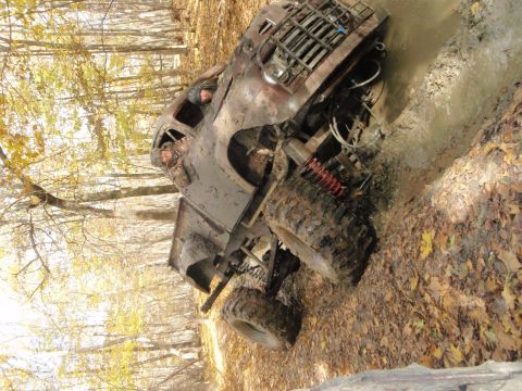 1990 Ford Bronco - This heavily modified off-road vehicle navigates a muddy path through a wooded area during autumn.