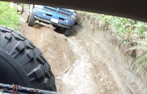 1982 Ford Bronco - A blue truck navigates a steep, muddy off-road trail.