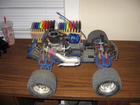 1992 Ford Ranger - Remote control nitro car with a blue engine cover and silver exhaust pipe sits on a wooden surface.
