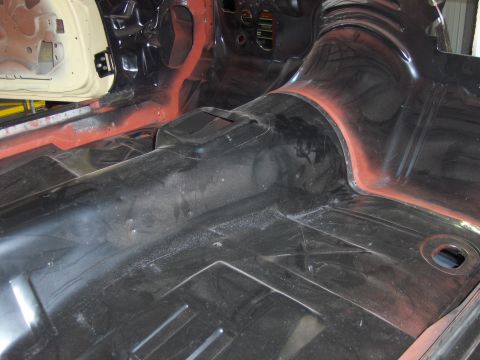 1970 Chevrolet Camaro - The bare interior floor of a car shows the transmission tunnel and surrounding metalwork, with some areas coated in red primer.