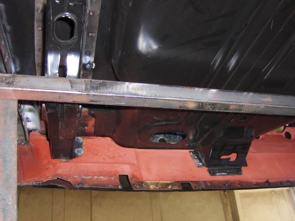 Undercarriage of a car with red primer and black metal components, viewed from below