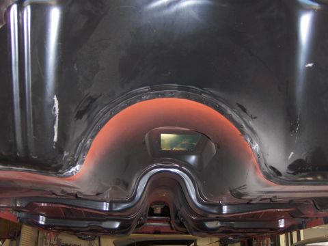 1970 Chevrolet Camaro - Underside view of a bare unibody floorpan on a lift, looking up at a freshly coated black transmission tunnel, driveshaft hump and rear sea…