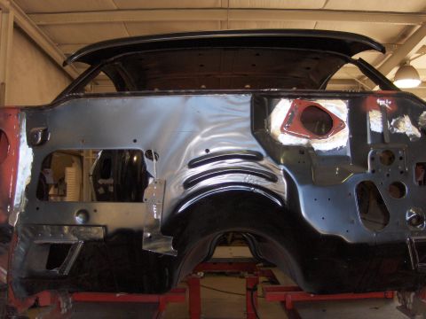 1970 Chevrolet Camaro - Bare unibody shell of a first-generation Camaro on a red frame rack in a shop, viewed head-on from the rear with the trunk lid open and the…