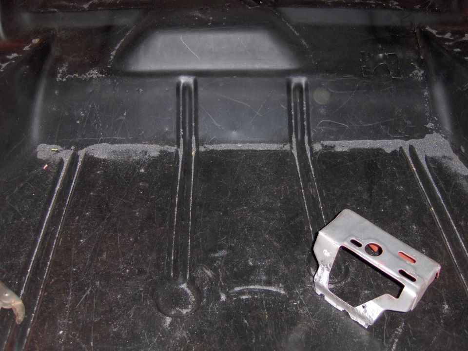 Trunk floor pan with two raised ribs and a small metal bracket on the right