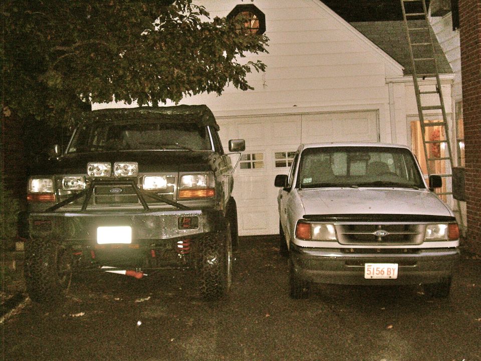 Front view of a black Ford F-150 with a brush guard and auxiliary lights, parked next to a white Ford Ranger