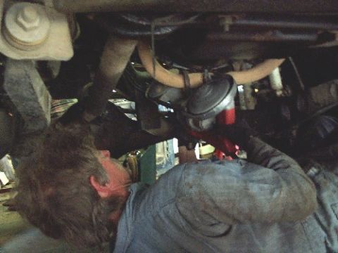 1982 Ford Bronco - A mechanic works on the underside of a vehicle, focusing on engine components.