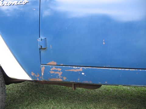1967 Ford Mustang - Close-up of a blue 1974 Ford Bronco door showing rust and a white stripe on the fender.