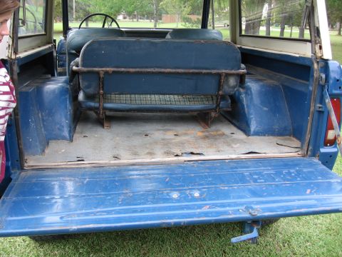 1967 Ford Mustang - The interior of a blue SUV, viewed from the open tailgate, reveals a rear bench seat and worn cargo floor.