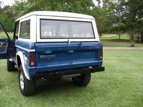 1967 Ford Mustang - Blue 1974 Ford Bronco with white top parked on grass.