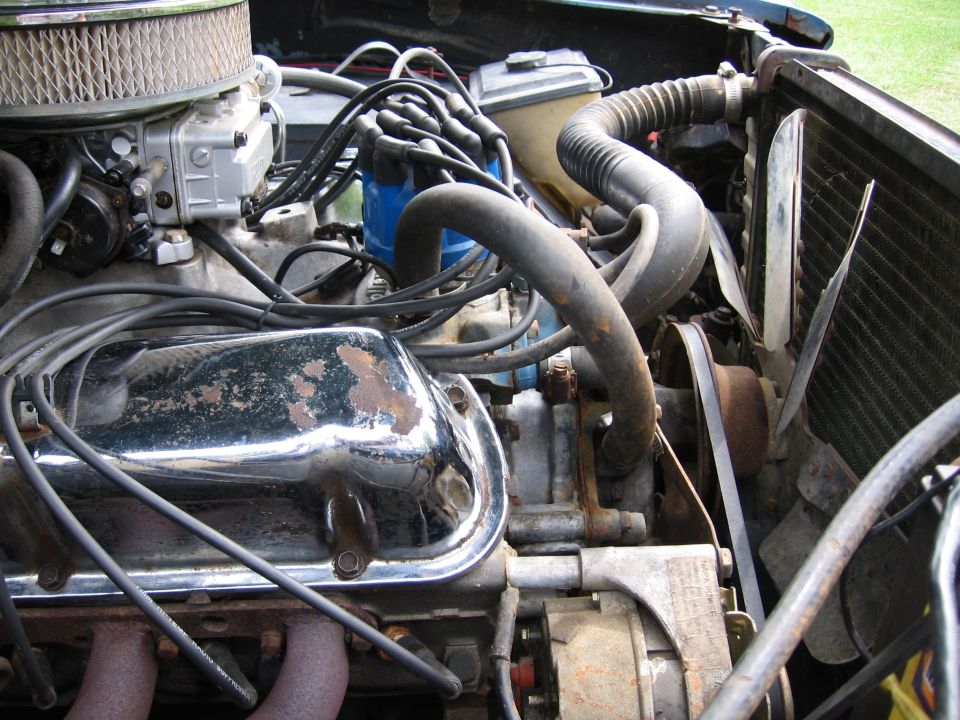 Close-up of a car's engine bay, showing the carburetor, distributor, and chrome valve cover