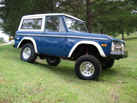 1967 Ford Mustang - This blue Ford Bronco features a white hardtop and is parked on a grassy area with trees in the background.
