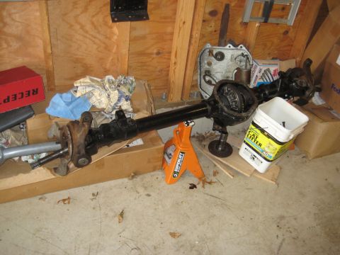 1995 Ford Bronco - An axle assembly, likely from a truck or SUV, is supported by jack stands in a cluttered garage setting.
