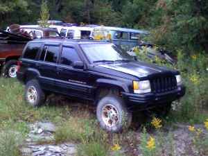 1996 Jeep Grand Cherokee - A black 1996 Jeep Grand Cherokee is parked in an outdoor setting with other vehicles visible in the background.