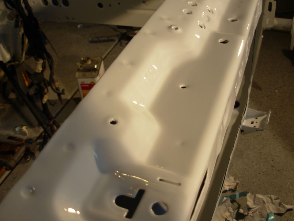 Close-up of a white painted car frame section with visible holes and indentations