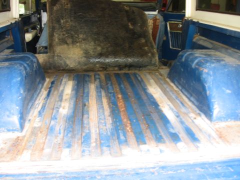1967 Ford Mustang - The interior of a blue vehicle shows a worn cargo bed with visible rust on the floor strips.