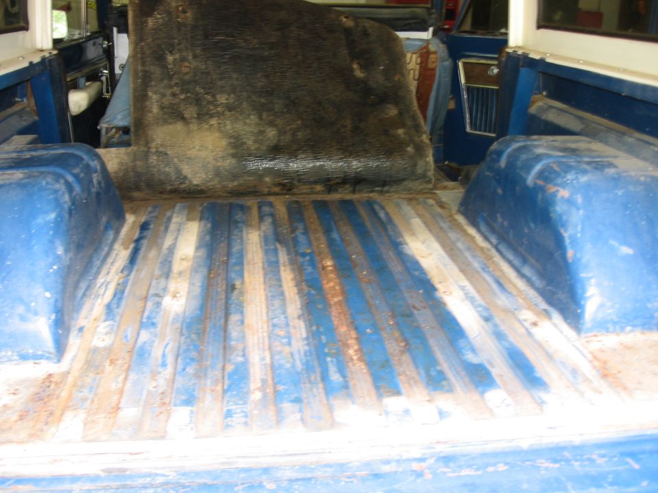 Rear cargo area of a blue vehicle with metal floor strips and a dirty mat