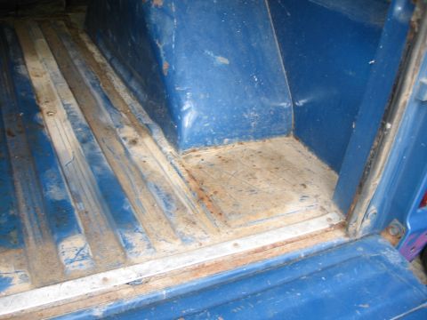 1967 Ford Mustang - The interior cargo area of a blue vehicle shows a ribbed floor with signs of wear and rust, along with a visible SUPERMOTORS logo.