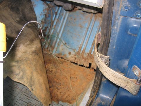 1967 Ford Mustang - The interior floor of a vehicle shows extensive rust damage and torn carpeting.
