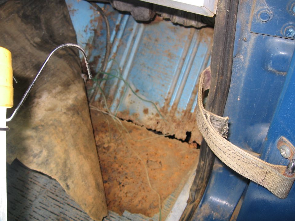 Blue interior floor with significant rust and torn carpet, showing exposed metal and wiring
