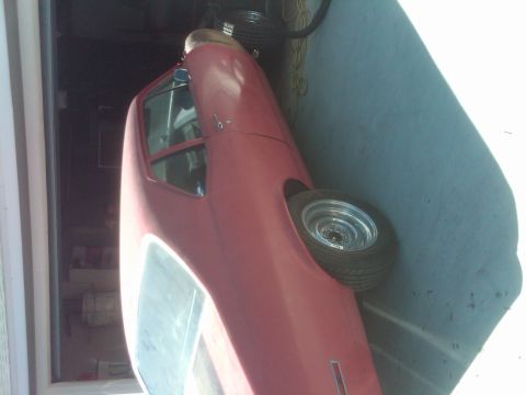 1982 Ford Bronco - A red coupe with chrome wheels is parked indoors, showing its side profile.