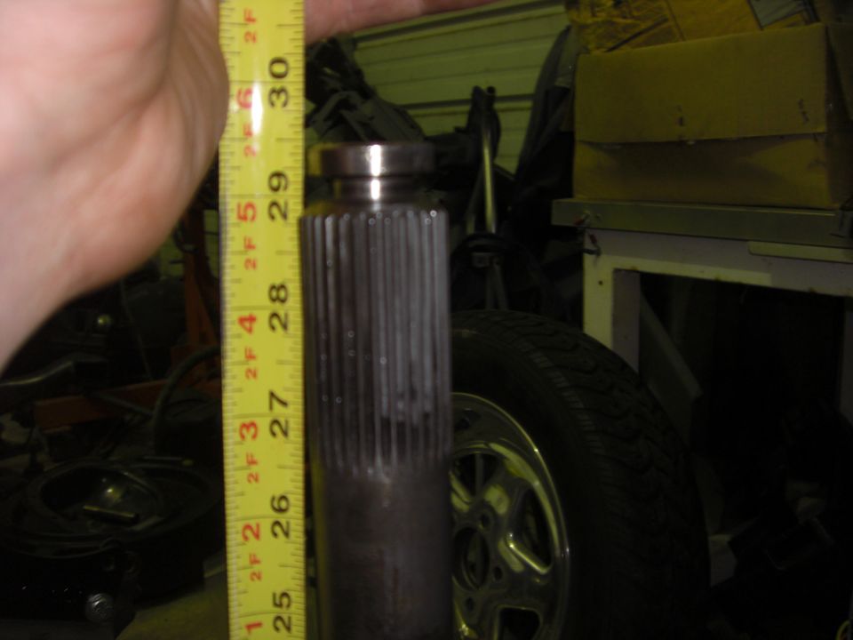 Measuring tape next to a splined shaft, with a tire and wheel in the background