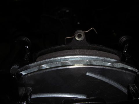 1988 Ford Bronco - Dark close-up looking down into a disc brake caliper, showing the brake pads with their steel backing plates seated against the rotor and a…