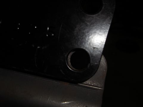 1988 Ford Bronco - Extreme close-up of the corner of a black-painted steel mounting bracket or plate, showing two drilled bolt holes and a rounded edge restin…