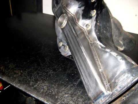 1996 Ford Bronco - A metal component with fresh welds sits on a dark, scratched surface.