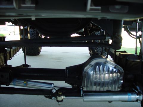 2001 Ford Excursion - Close-up view of the undercarriage, highlighting dual stabilizer shocks and a polished differential cover, with visible "SUPERMOTORS" text.