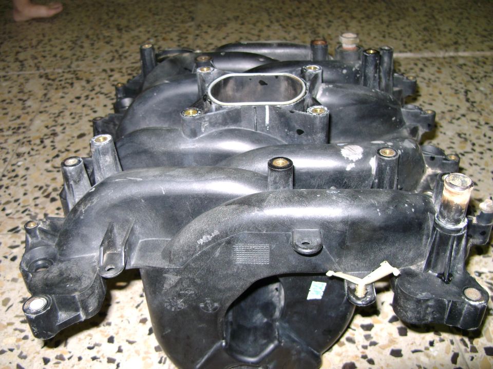 Black plastic intake manifold with various ports and mounting points