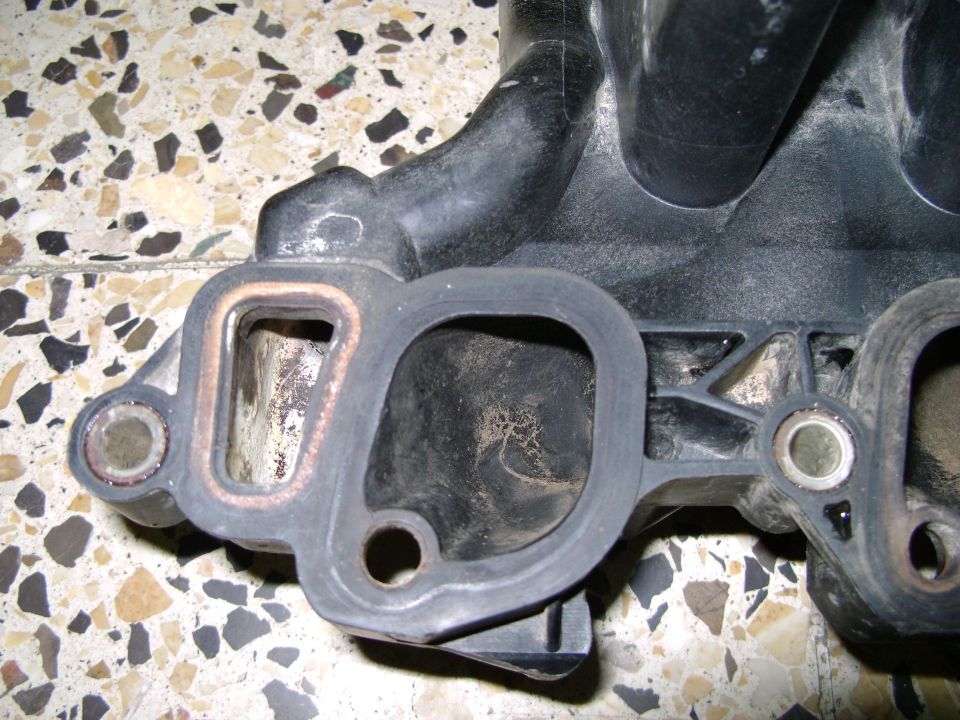 Close-up of a black plastic intake manifold part with gasket material visible