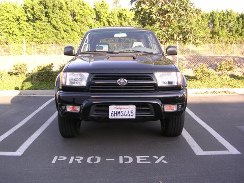 2000 Toyota 4Runner - This black Toyota 4Runner is parked in a lot with trees in the background.