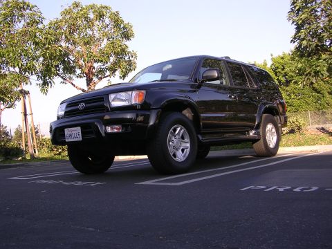 2000 Toyota 4Runner - This black 2000 Toyota 4Runner is parked in a lot with trees in the background.