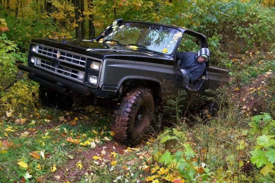 Black SUV tilted on a muddy trail with a person leaning out the door. Off-road tires are visible