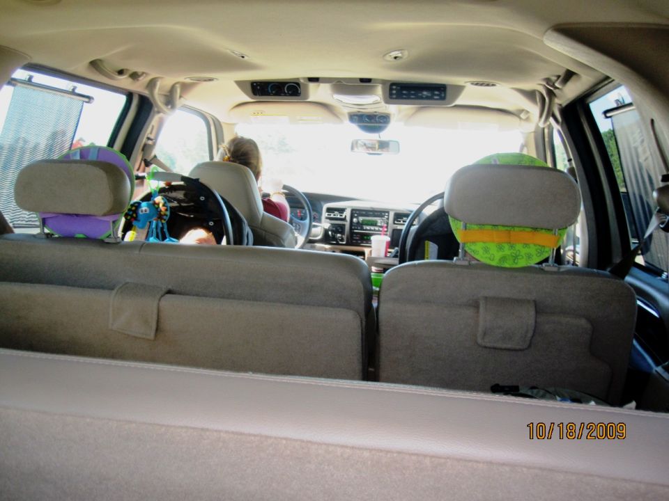 View from rear cargo area of Ford Excursion interior with tan seats, kids' toys on headrests, driver up front