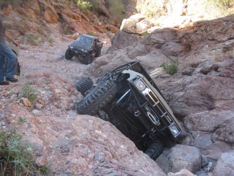 1986 Toyota Hilux - Two off-road trucks navigate a treacherous rocky canyon trail, with one vehicle overturned.