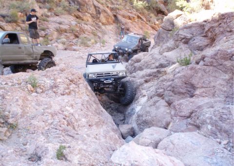 1986 Toyota Hilux - Multiple off-road vehicles traverse a challenging rocky terrain in a desert canyon.