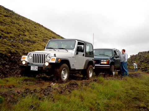 1996 Ford Bronco - Two SUVs navigate a , grassy terrain under an overcast sky.