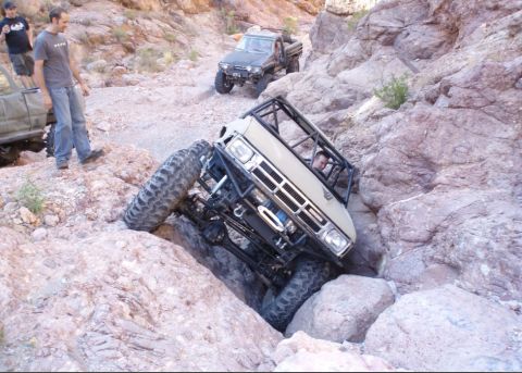 1986 Toyota Hilux - Modified pickup truck attempts to traverse a difficult rocky terrain, with another truck visible in the background.